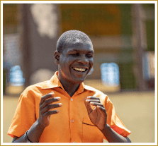 A blind Ghanaian man in an orange shirt smiles enthusaistically