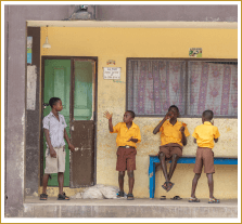 Three young Ghanaian students in bright orange line up smiling against a wall and one in grey comes out of a green door and looks at his waving peer